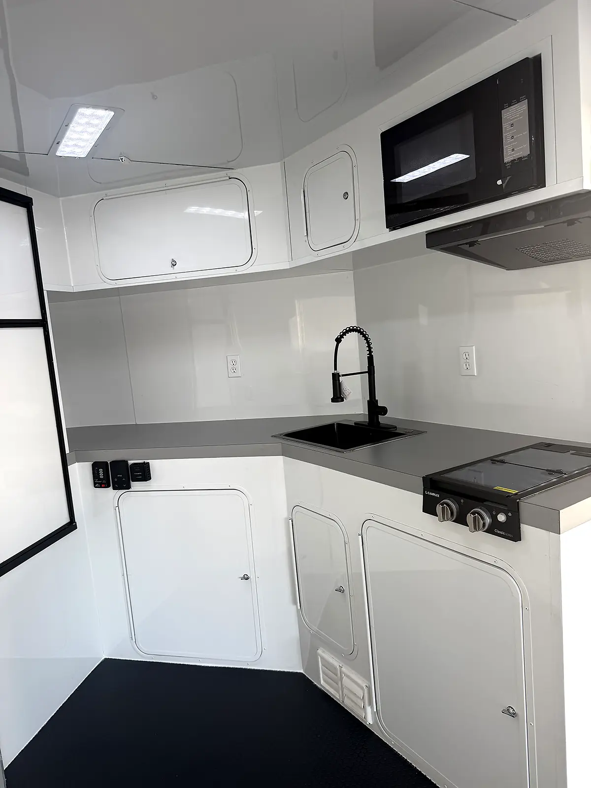 Living quarters kitchenette with sink, stove, microwave and white cabinets
